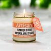 The artisan kitchen summer citrus candle in a glass jar lit sitting on a white marble countertop